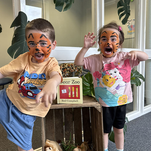 Two children with tiger face paint pose beside a zoo-themed display featuring Dear Zoo book,