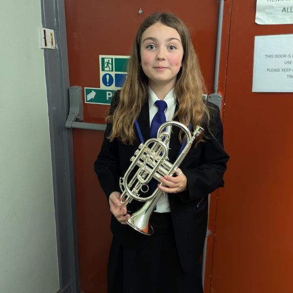 Child in school uniform holding a silver trumpet