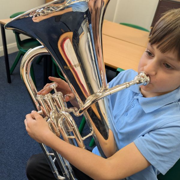 Child seated in a classroom, playing a large brass instrument
