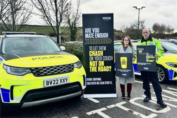 Police vehicle and roadside sign promoting safe crossing.